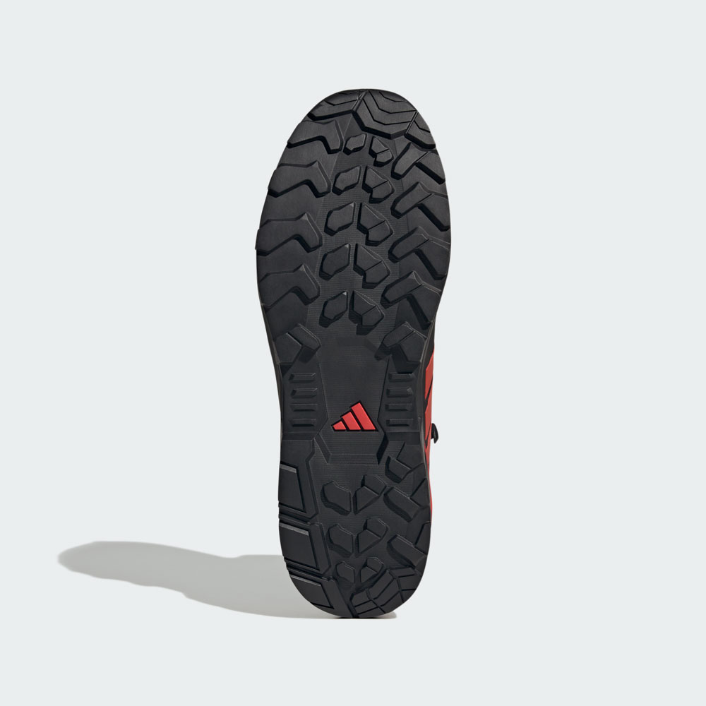 Unteransicht der schwarzen Gripsohle eines adidas Outdoor-Schuhs mit rotem Obermaterial und markantem Profilmuster für optimalen Halt im Gelände