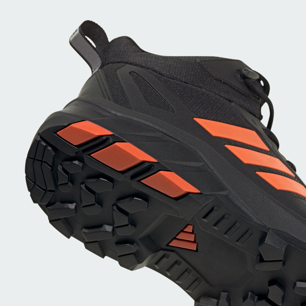 Nahaufnahme der robusten Außensohle eines schwarzen Adidas Trail-Schuhs mit orangefarbenen Akzenten und griffigem Profil