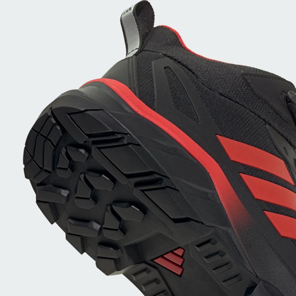 Nahaufnahme der robusten Profilsohle eines adidas Trailrunning-Schuhs in Schwarz mit roten Akzenten und charakteristischen Seitenstreifen