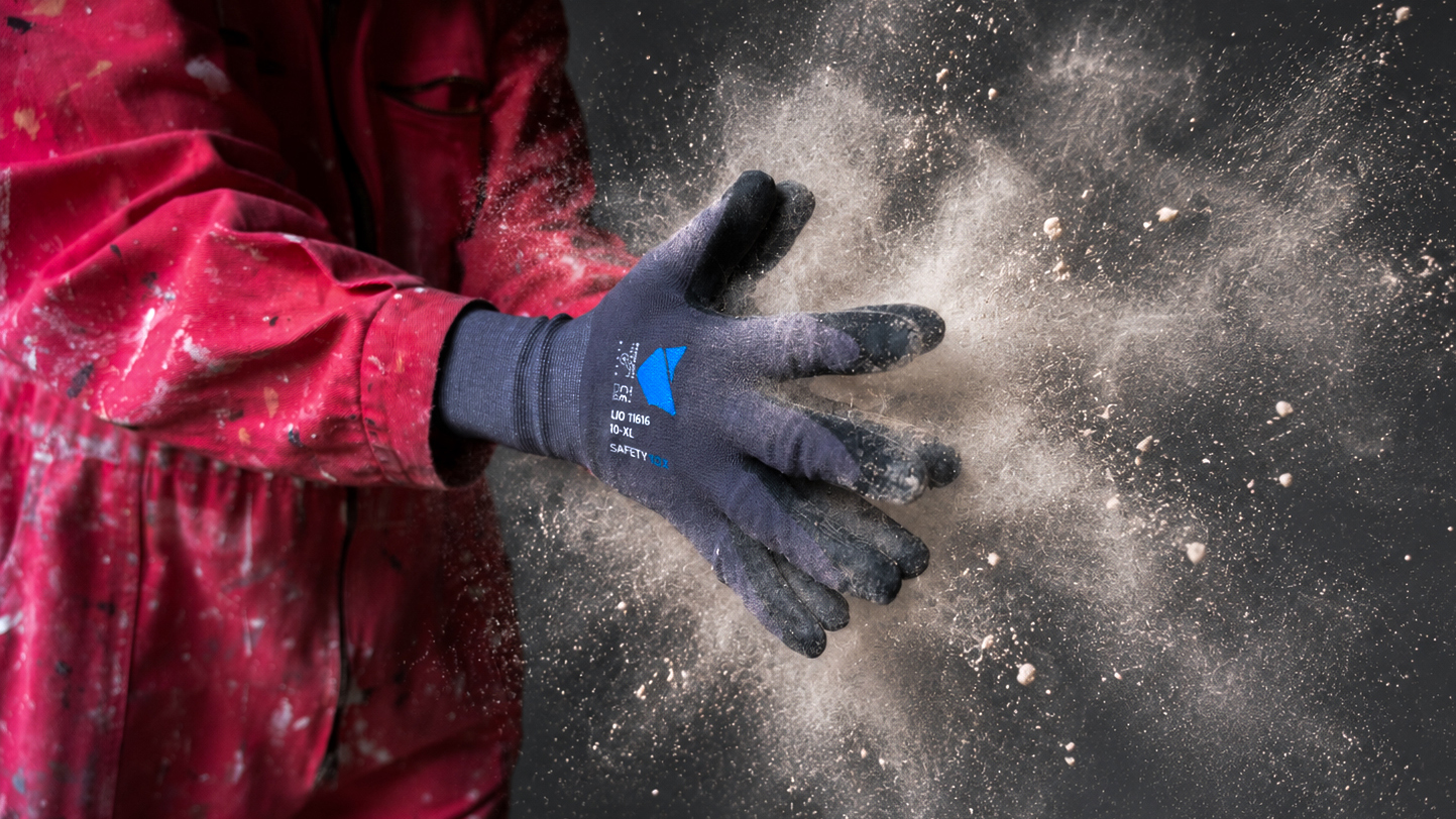Person in roter Arbeitsjacke klatscht in die Hände mit grauem Safety Tox Arbeitshandschuh, wodurch Staub aufwirbelt