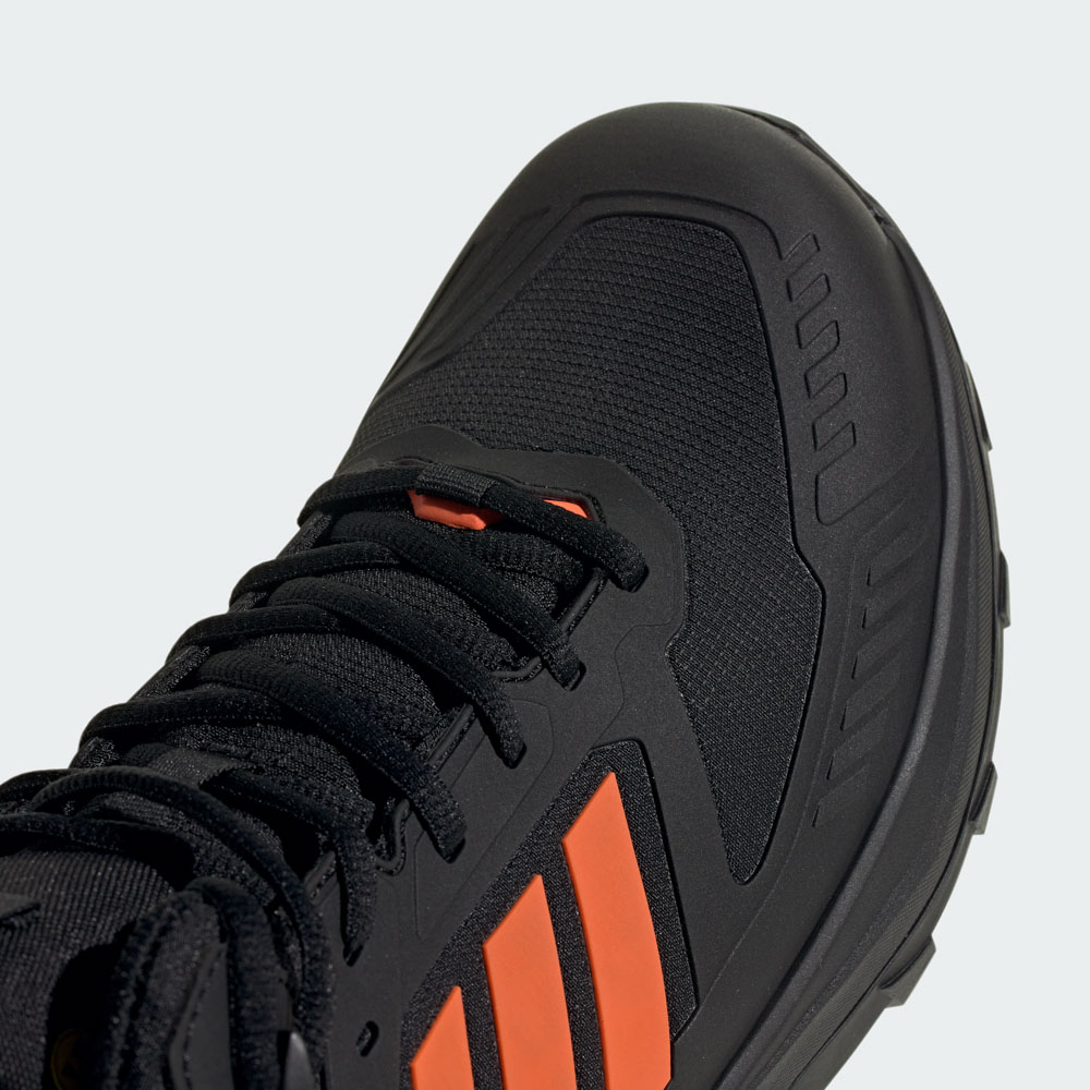 Nahaufnahme eines schwarzen adidas Sneakers mit orangefarbenen Akzentstreifen, Schnürsenkeln und robuster Sohle