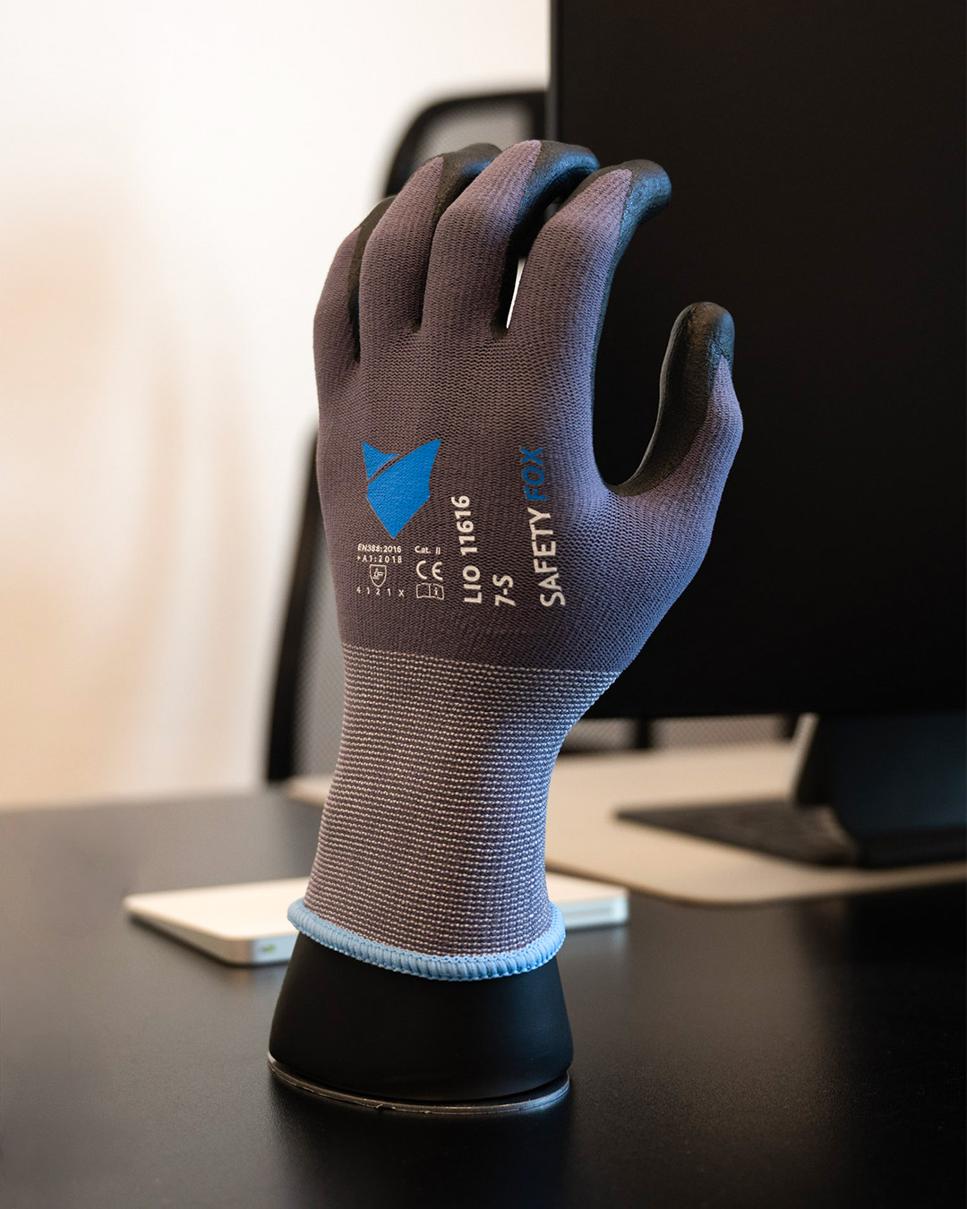 Grauer Safety Fox Arbeitshandschuh LIO 11616 mit schwarzer PU-Beschichtung an Fingern und Handfläche, präsentiert auf einer Handform im Büro