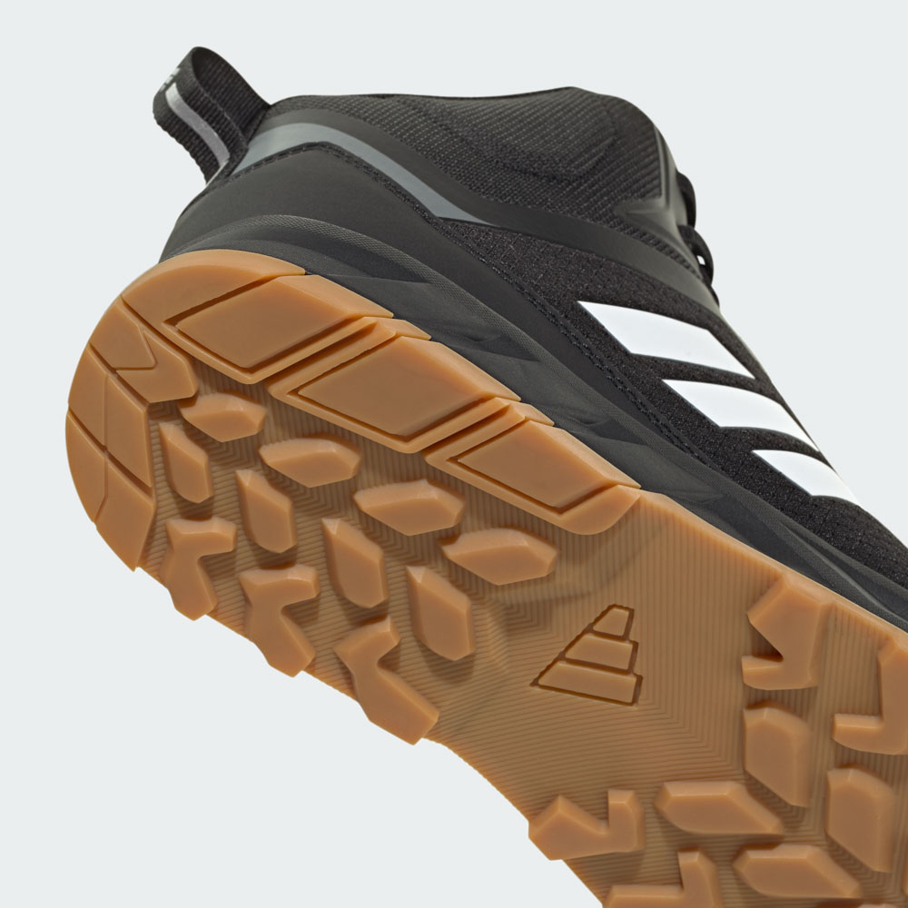 Nahaufnahme der Ferse eines schwarzen adidas Trail-Schuhs mit grobstolliger Gummisohle in Gum-Braun und weißen Markenstreifen
