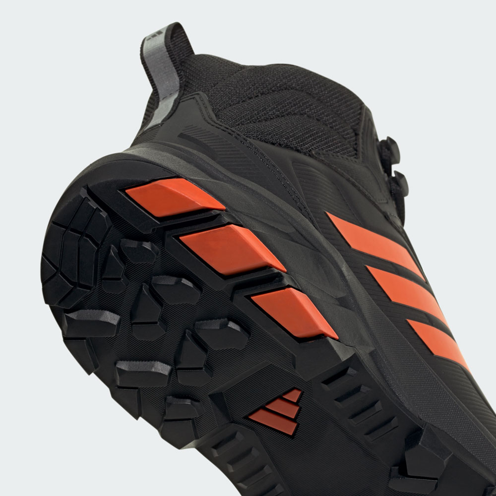 Nahaufnahme der robusten Gummisohle eines schwarzen Adidas Outdoor-Schuhs mit markantem Profil und orangefarbenen 3-Streifen-Akzenten